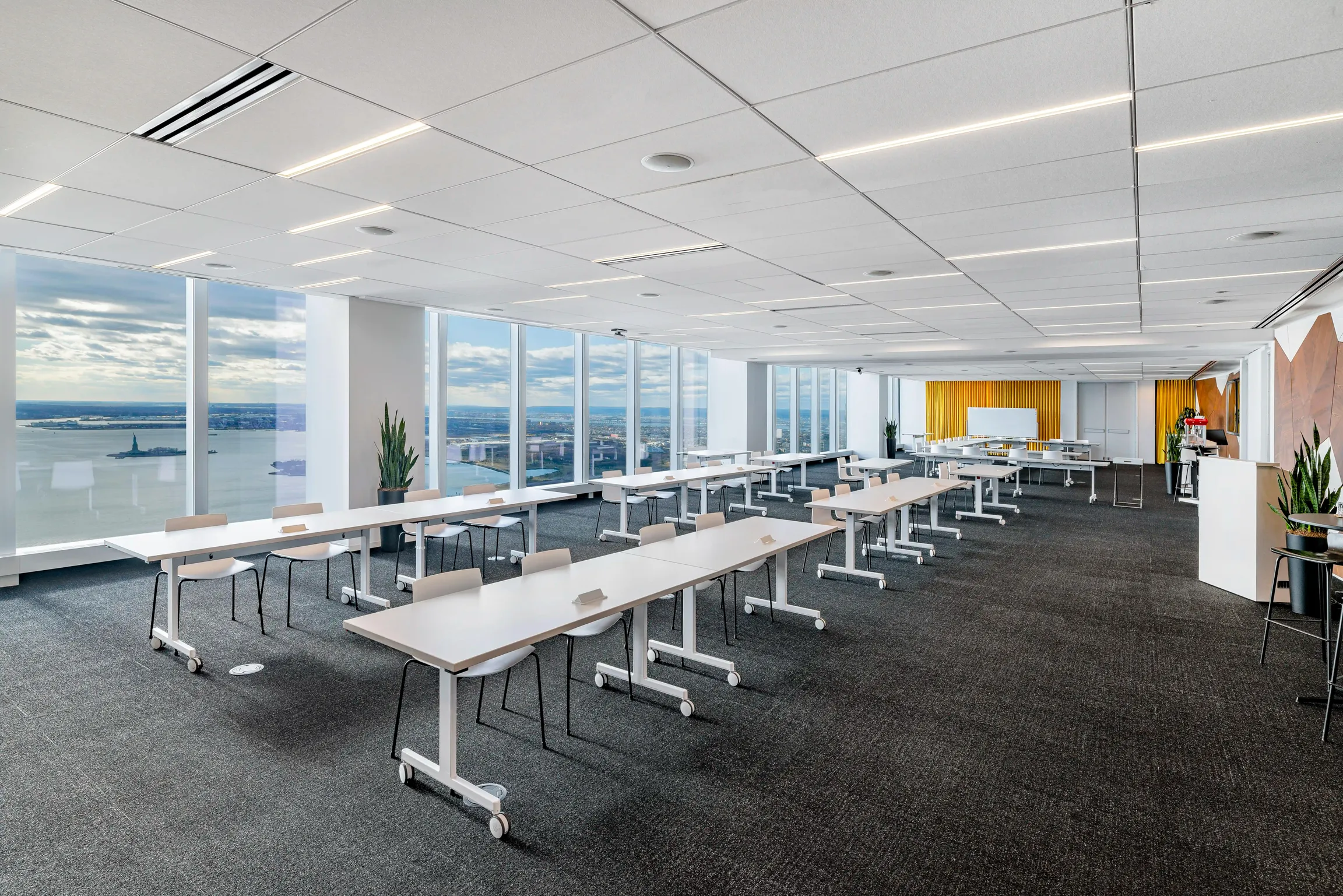 A spacious open conference or event space with rows of tables and chairs with a view of the Statue of Liberty. One of Well& by Durst's offerings at One World Trade Center.