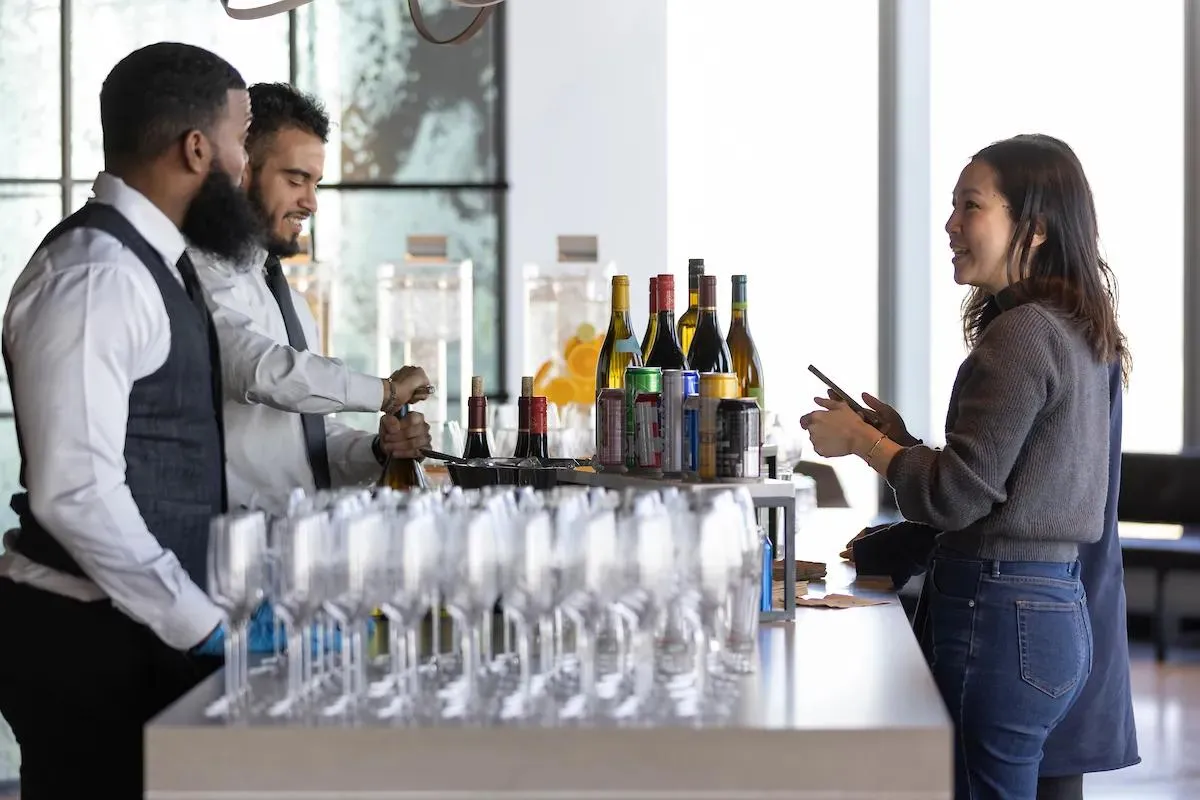 A woman standing at a bar filled with champagne glasses and wine bottles at an corporate event at Well& by Durst at One World Trade Center..