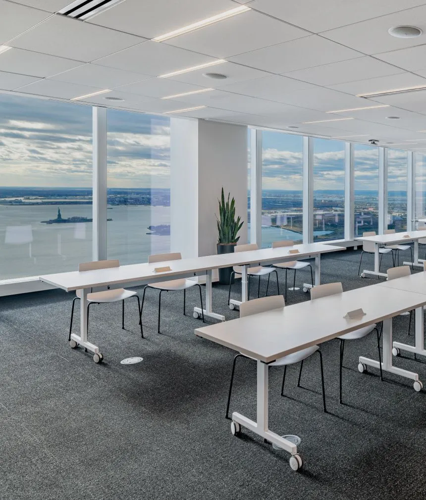 A spacious open conference or event space with rows of tables and chairs with a view of the Statue of Liberty. One of Well& by Durst's offerings at One World Trade Center.