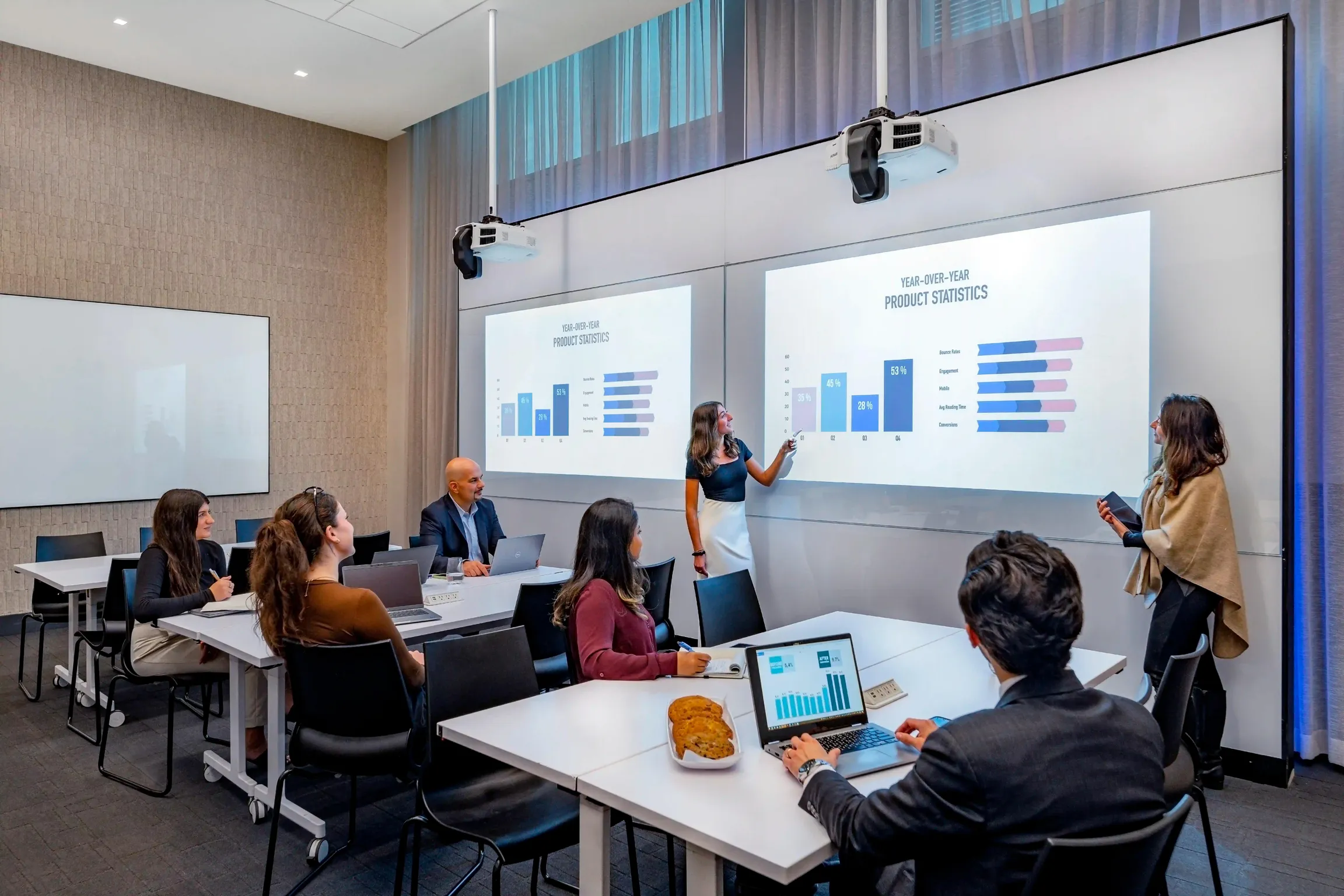 Professionals in an NYC meeting conference space watching two presenters pointing to graphs projected onto a screen at Well& by Durst.