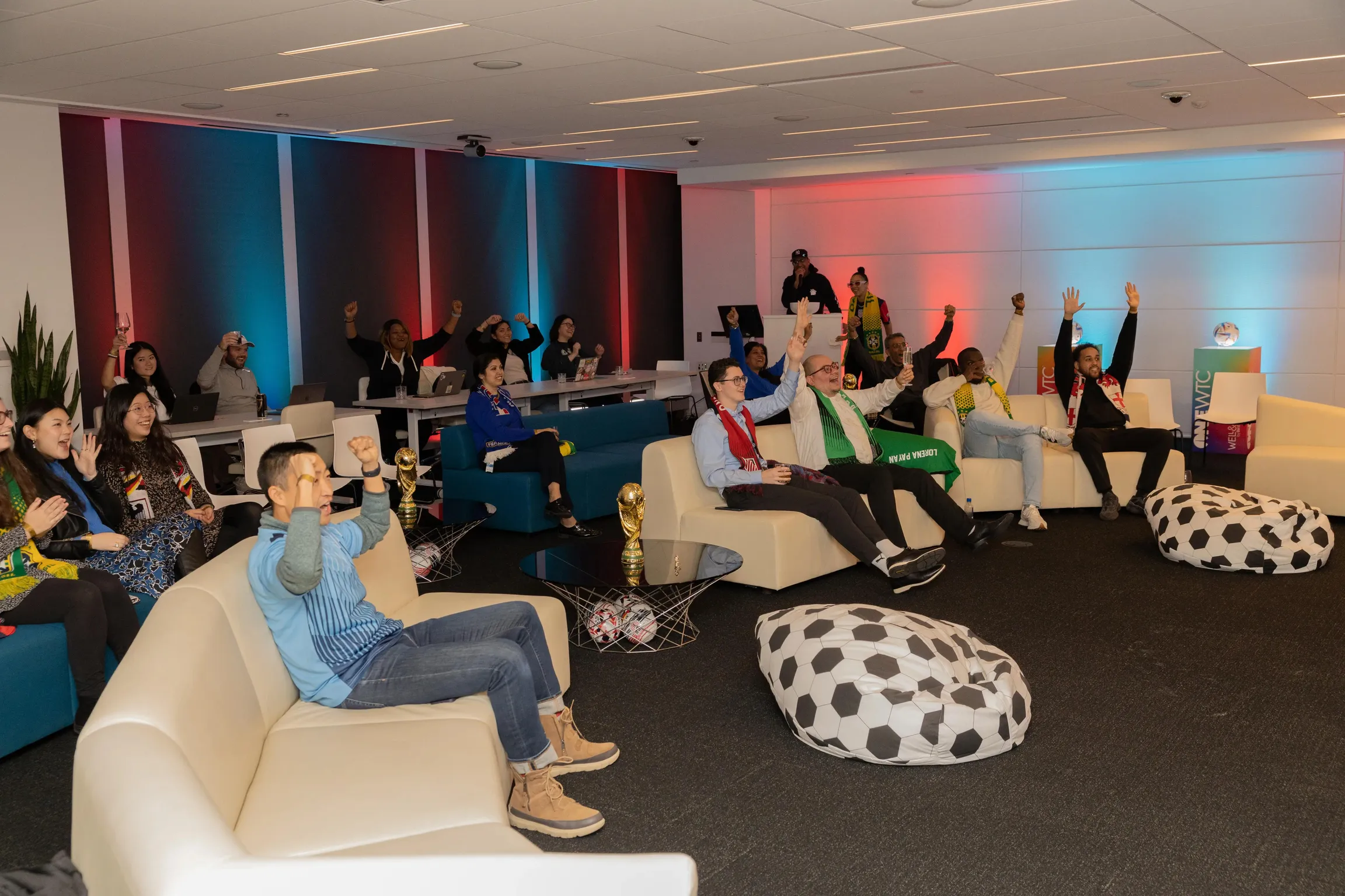 A diverse group of professionals sitting in a decorative lounge at an event watching the World Cup on a screen.