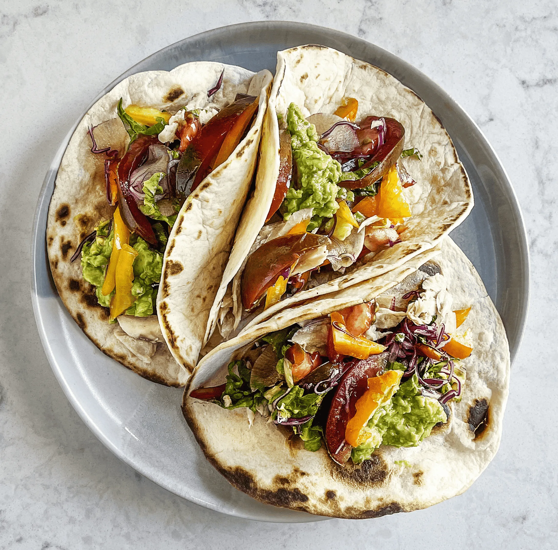 Three wraps are neatly arranged on a plate. Each wrap is filled with grilled chicken, fresh lettuce, diced tomatoes, and a creamy sauce, all wrapped in soft, warm tortillas.