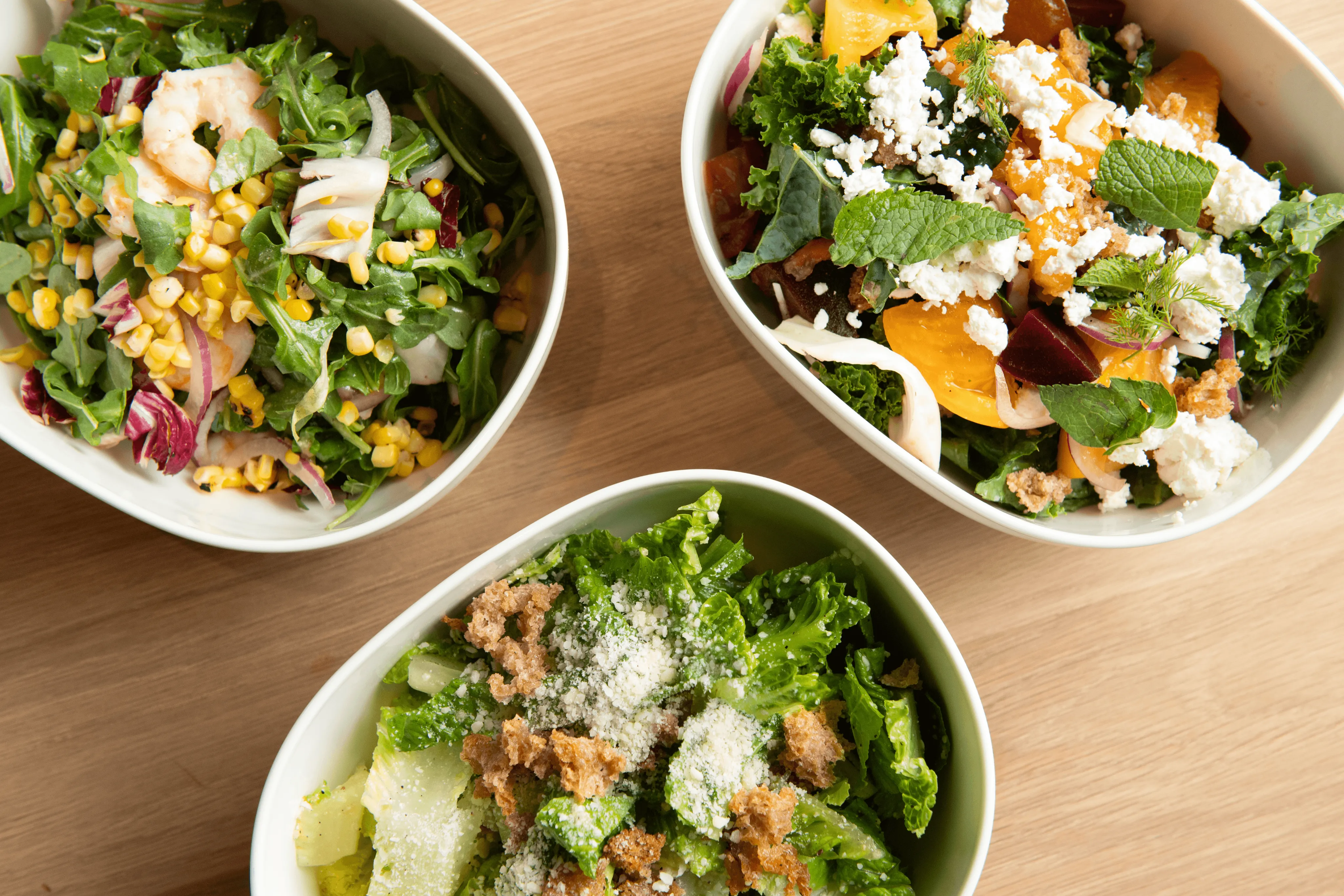 Three bowls of fresh Romaine salad topped with crispy bread crumbs, crumbled feta cheese, and a variety of herbs. Displayed in an appetizing and colorful presentation.