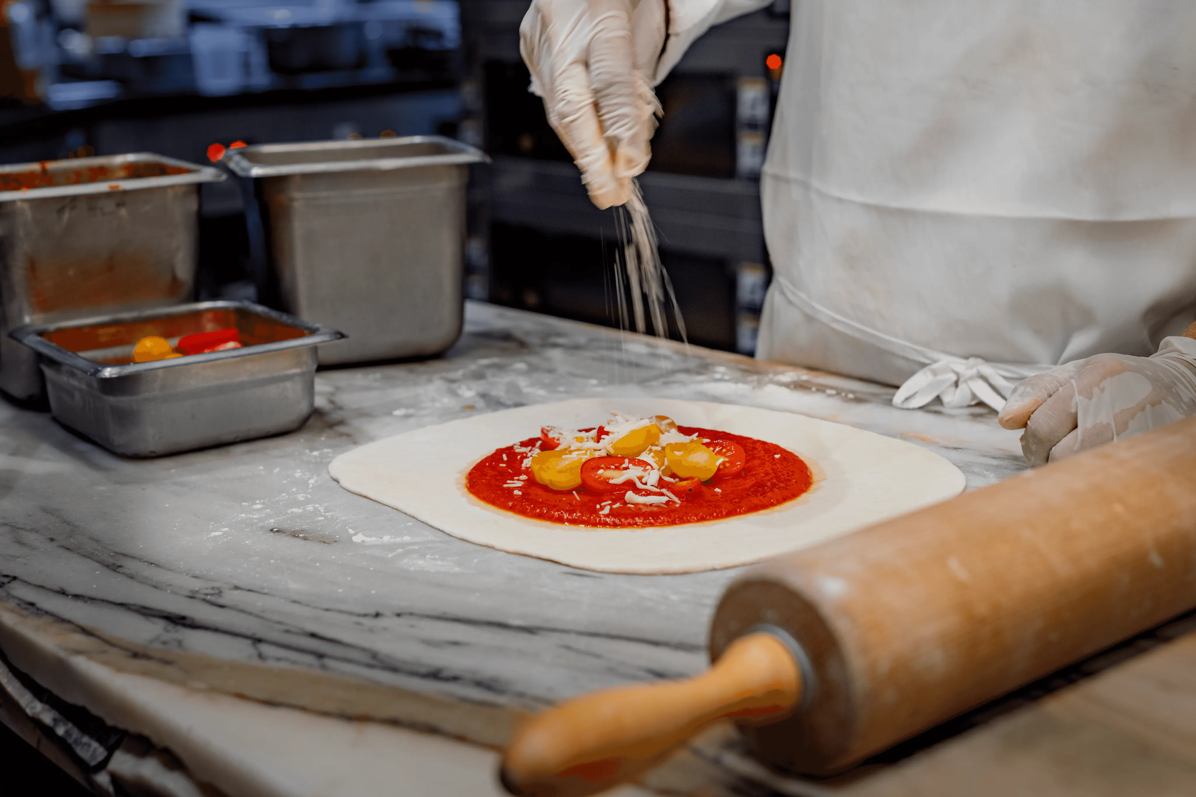 Pizza chef flattening dough on a kitchen surface.