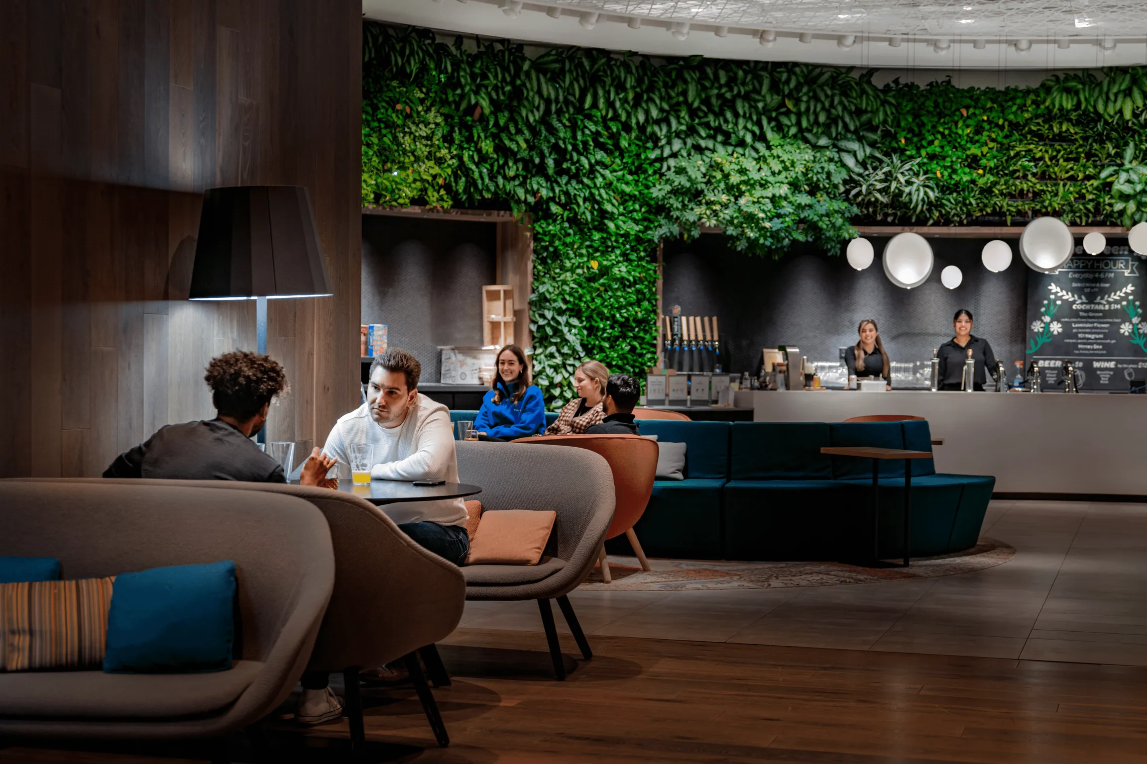 A bustling modern lobby with people seated at tables and chairs, engaged in conversation
