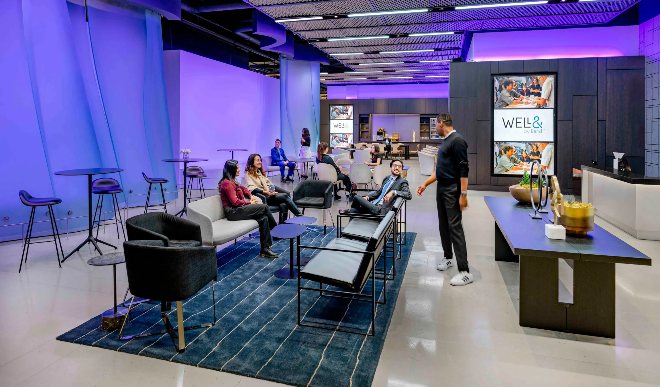 Amenities space in 151 West 42nd, people gathered, screens showing the "Well& by Durst" logo on it.