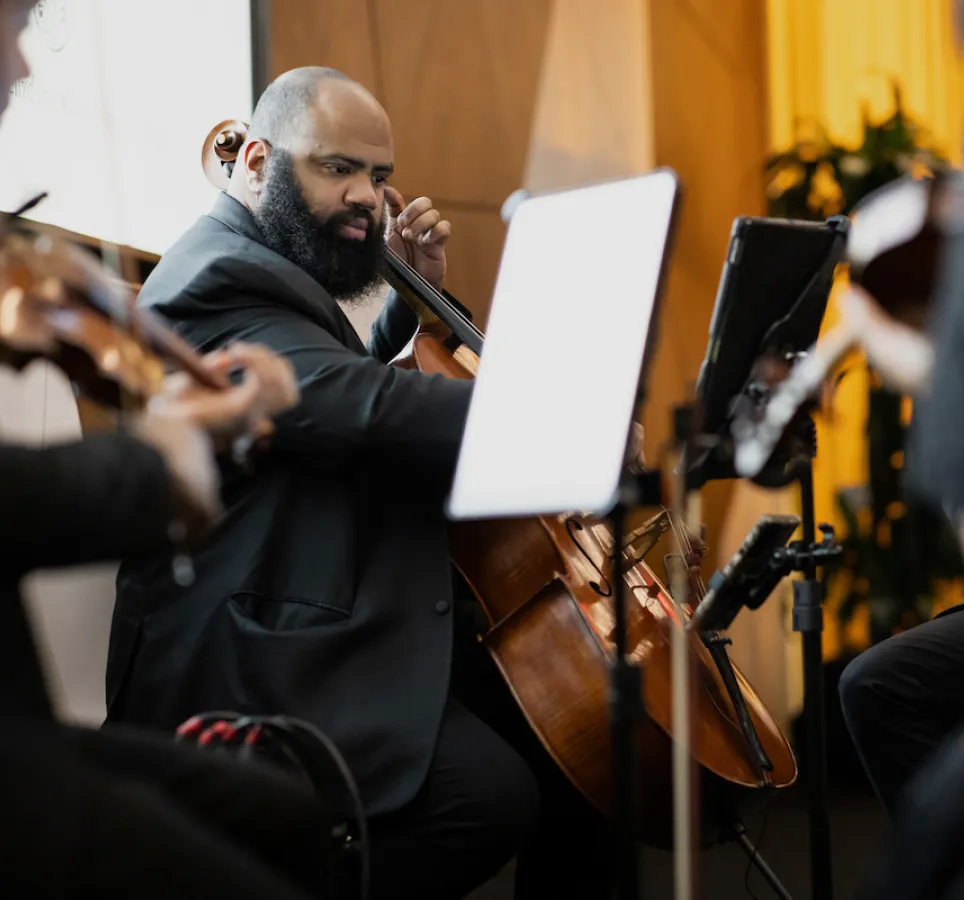 A man in a suit playing the violin, surrounded by other musicians and musical instruments.