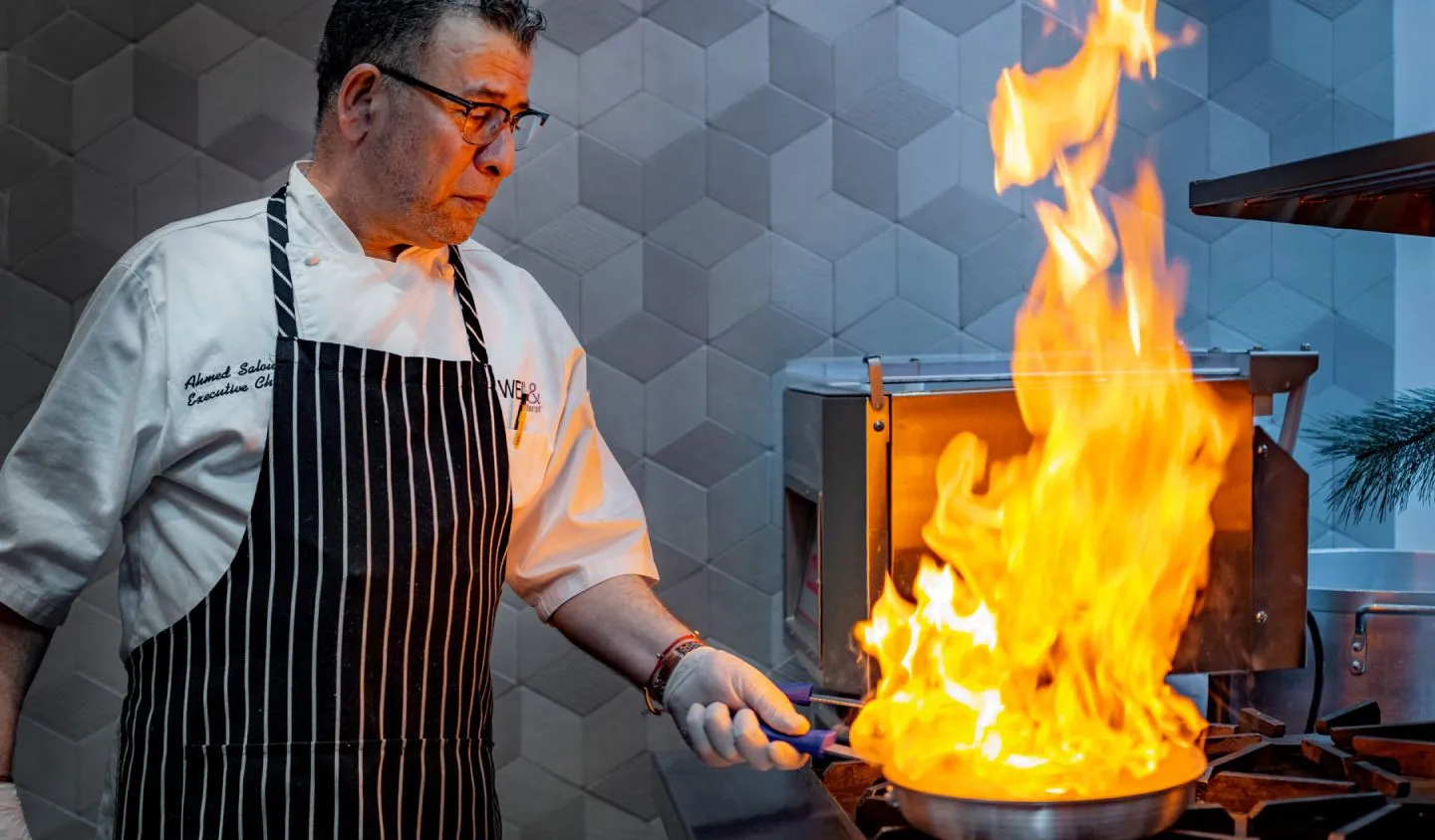 A man in a chef's apron cooking over an open flame.