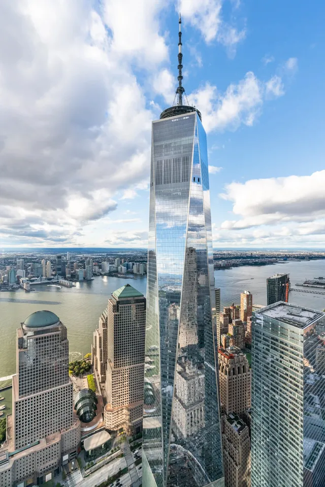 One World Trade Center—an iconic skyscraper in New York City. It stands out tall with its glass facade which reflects the surrounding buildings and water.