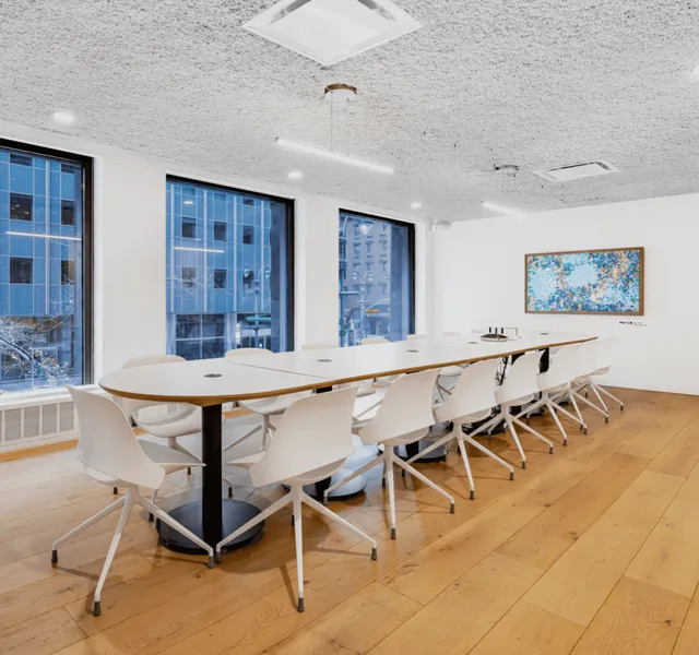 A long table in a well-lit conference room with windows showing a white office building.